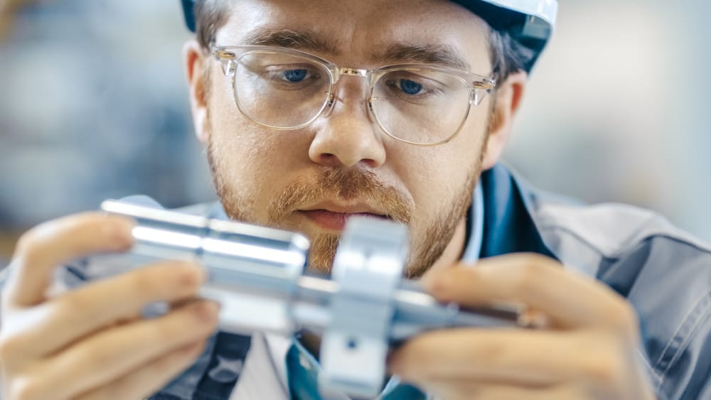 Mechanical engineer with glasses and hard hat connecting two components.