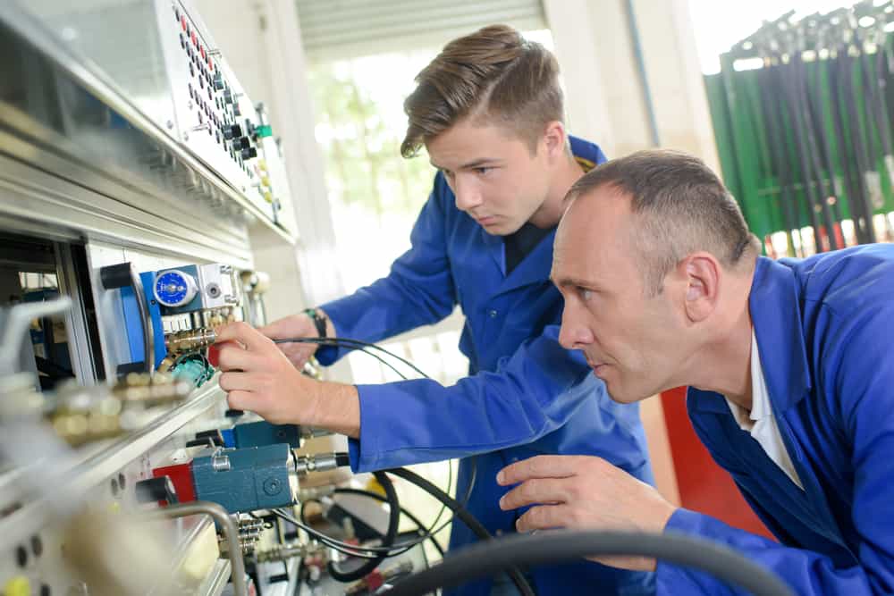 Mechanical engineer with apprentice working in a factory.