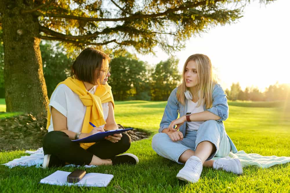 Social worker talking to teenage student on the lawn in the park.