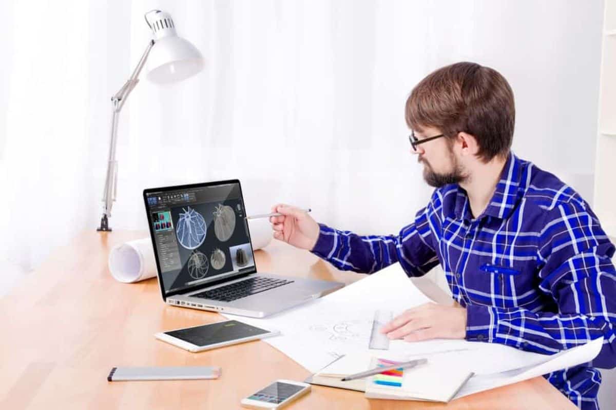 Man looking at his laptop with concept graphs on screen while holding a ruler on draft papers.