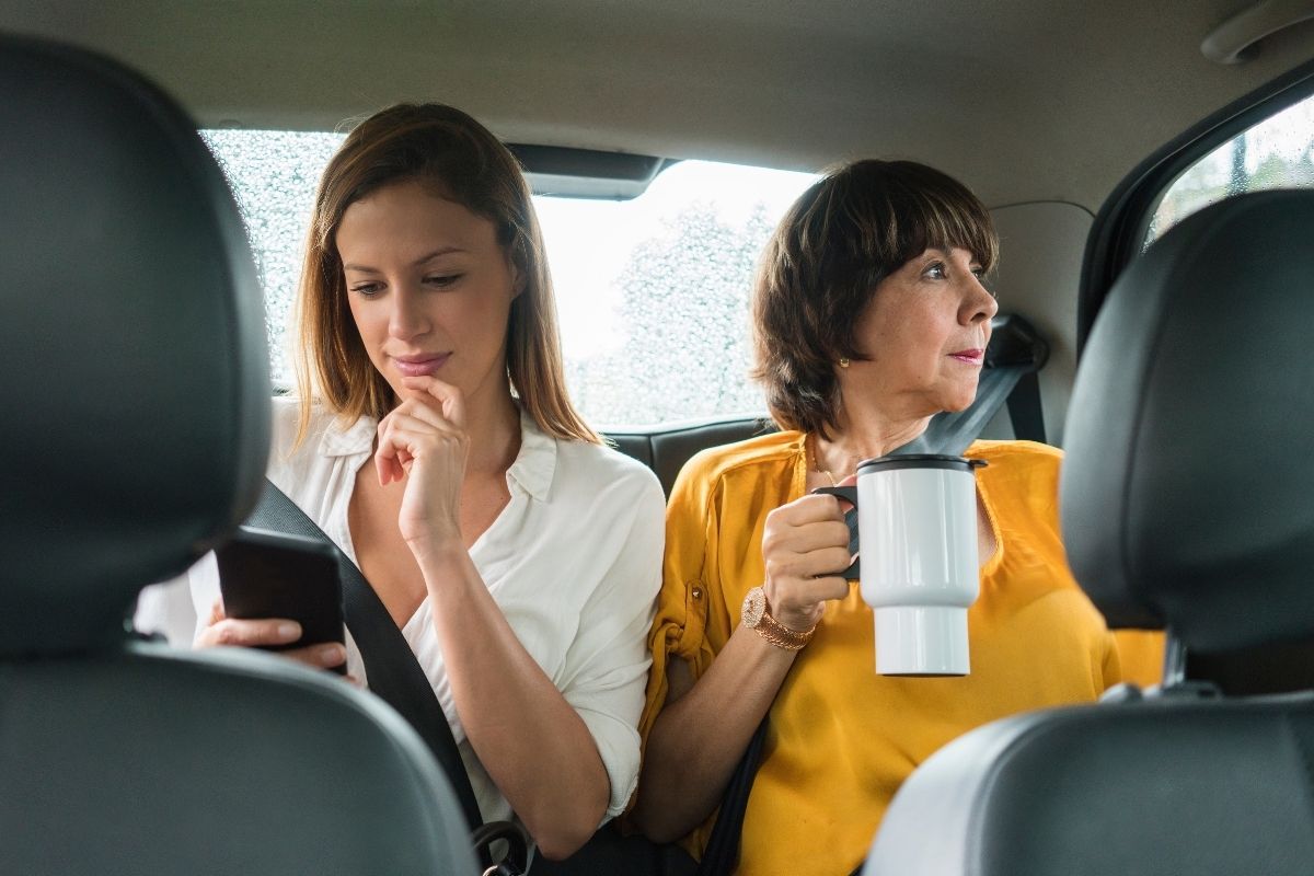 2 latin women ride in a uber taxi while drinking coffee.