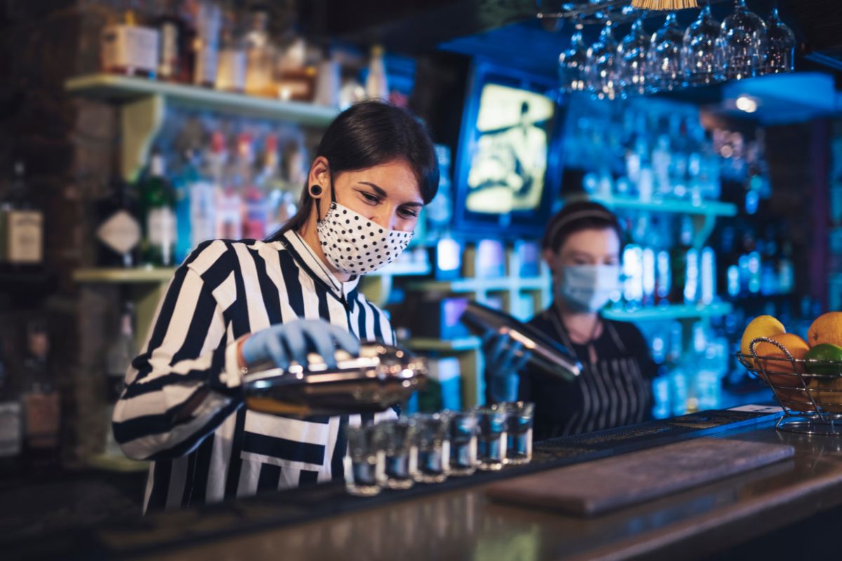 Bartender woman working with protective face mask at the bar.