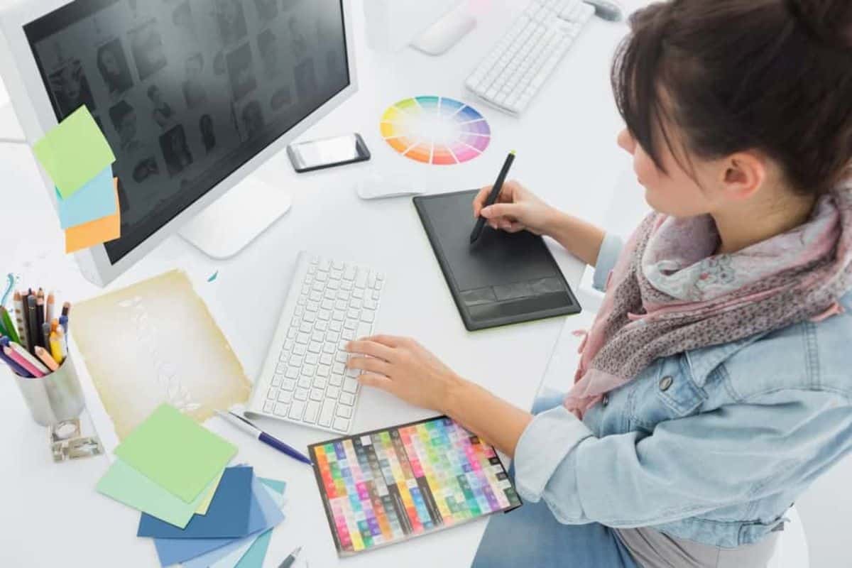 Woman sketching on a drawing pad while looking at a computer monitor on her workstation.