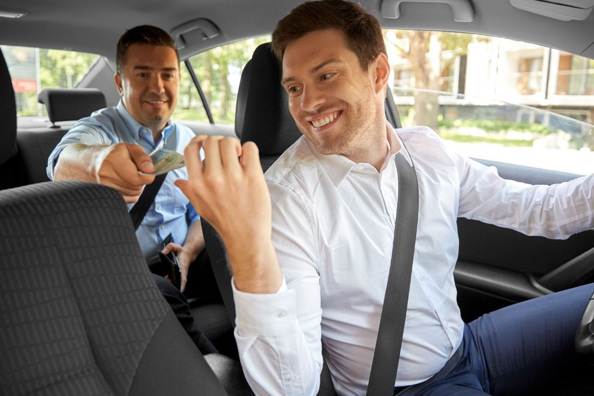 A passenger pays his uber driver with cash.