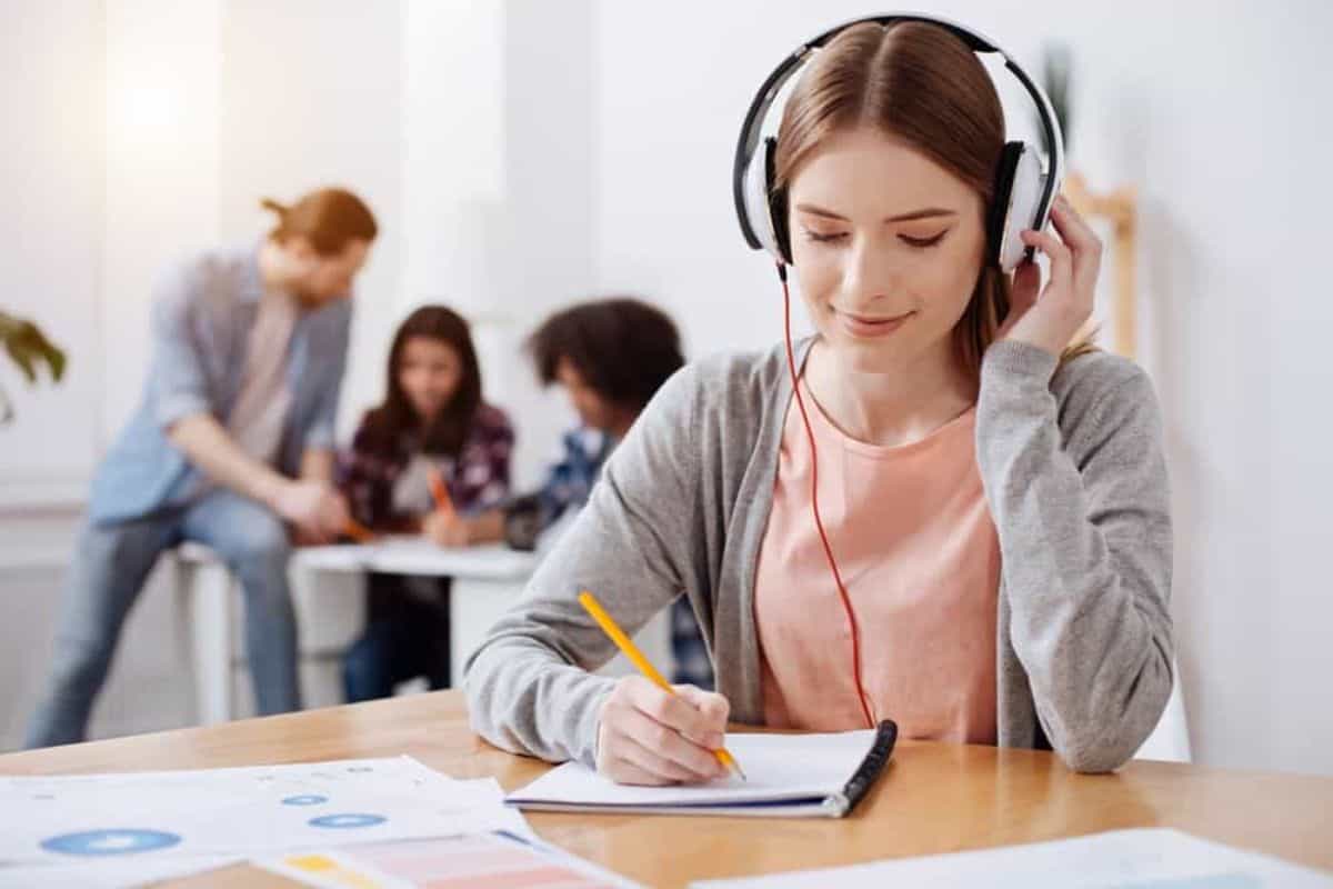 Young woman wearing a headphone while writing on a notebook.