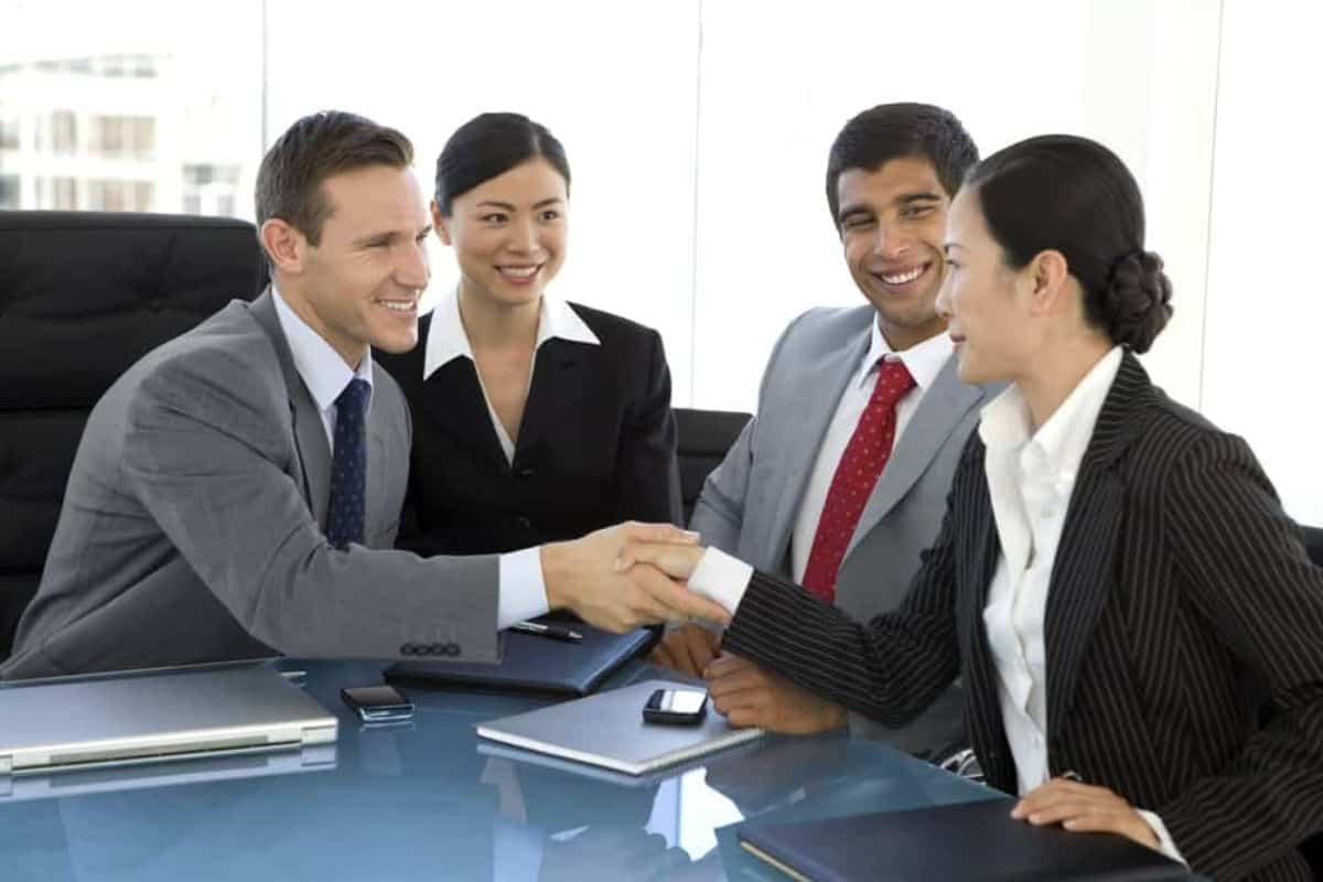 Businessman and woman shaking hands with another pair of woman and man in suit between them.