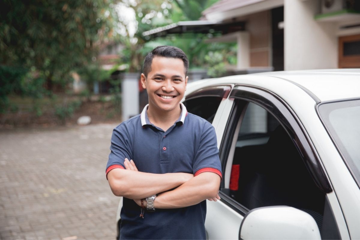 Young Asian man crossed arm standing in front of his car.