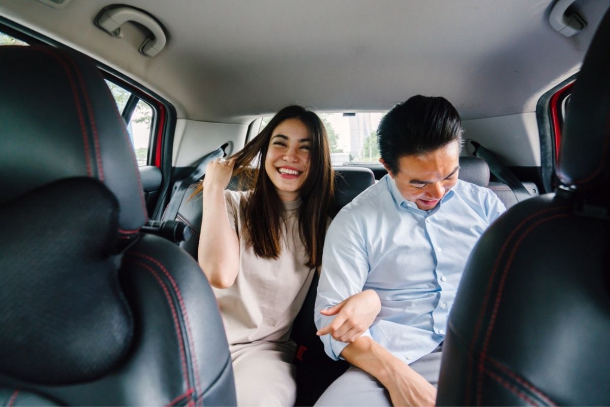 A young and attractive Asian couple sit together in the backseat of a car as they are driven to their destination. 